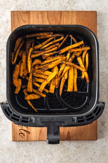 A black air fryer basket filled with air fried butternut squash fries.