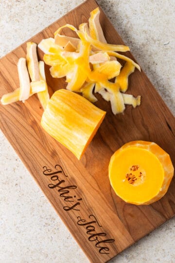 A butternut squash peelt and cut in half width wise on a wooden cutting board.