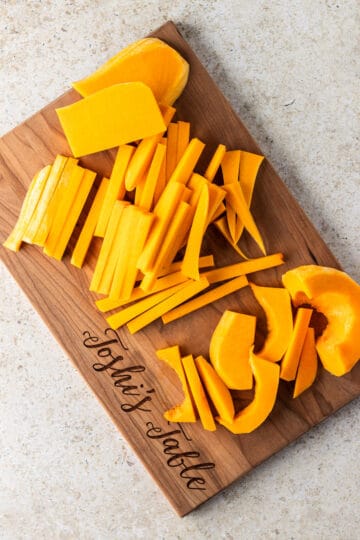 A butternut squash cut into planks and fries on a wooden cutting board.