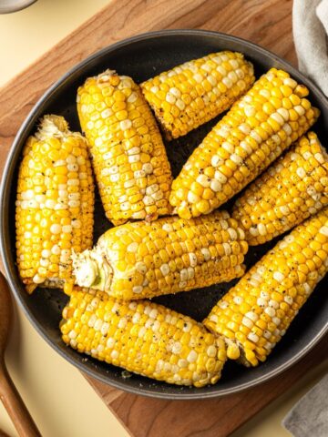 Air Fried corn on the cob in a black bowl on a wooden cutting board topped with salt and black pepper.