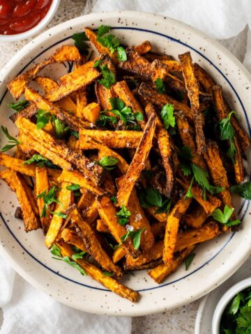 An overhead view of a large plate of air fried butternut squash fries garnished with fresh parsley.