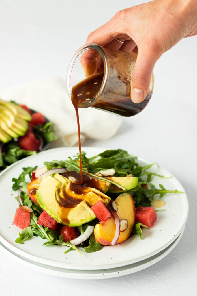 Balsamic dressing being poured on peach watermelon salad