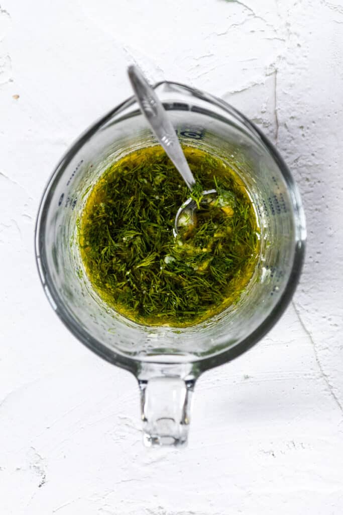 Liquid measuring cup with lemon dill dressing and a spoon.