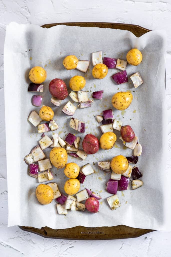 Mini potatoes and red onions on a baking sheet.
