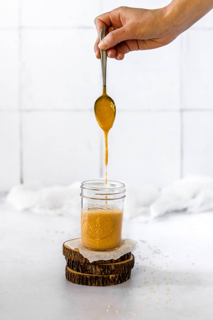 Maple miso tahini dressing dripping off a spoon into a mason jar.