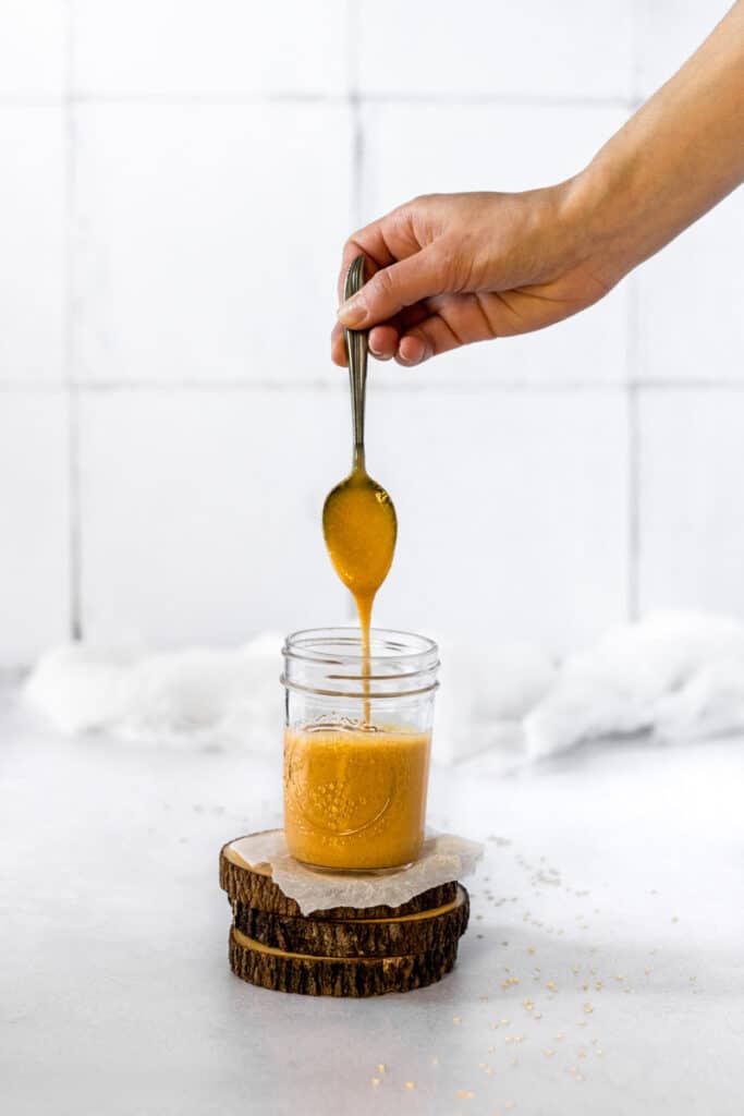 Maple miso tahini dressing dripping off a spoon into a mason jar.