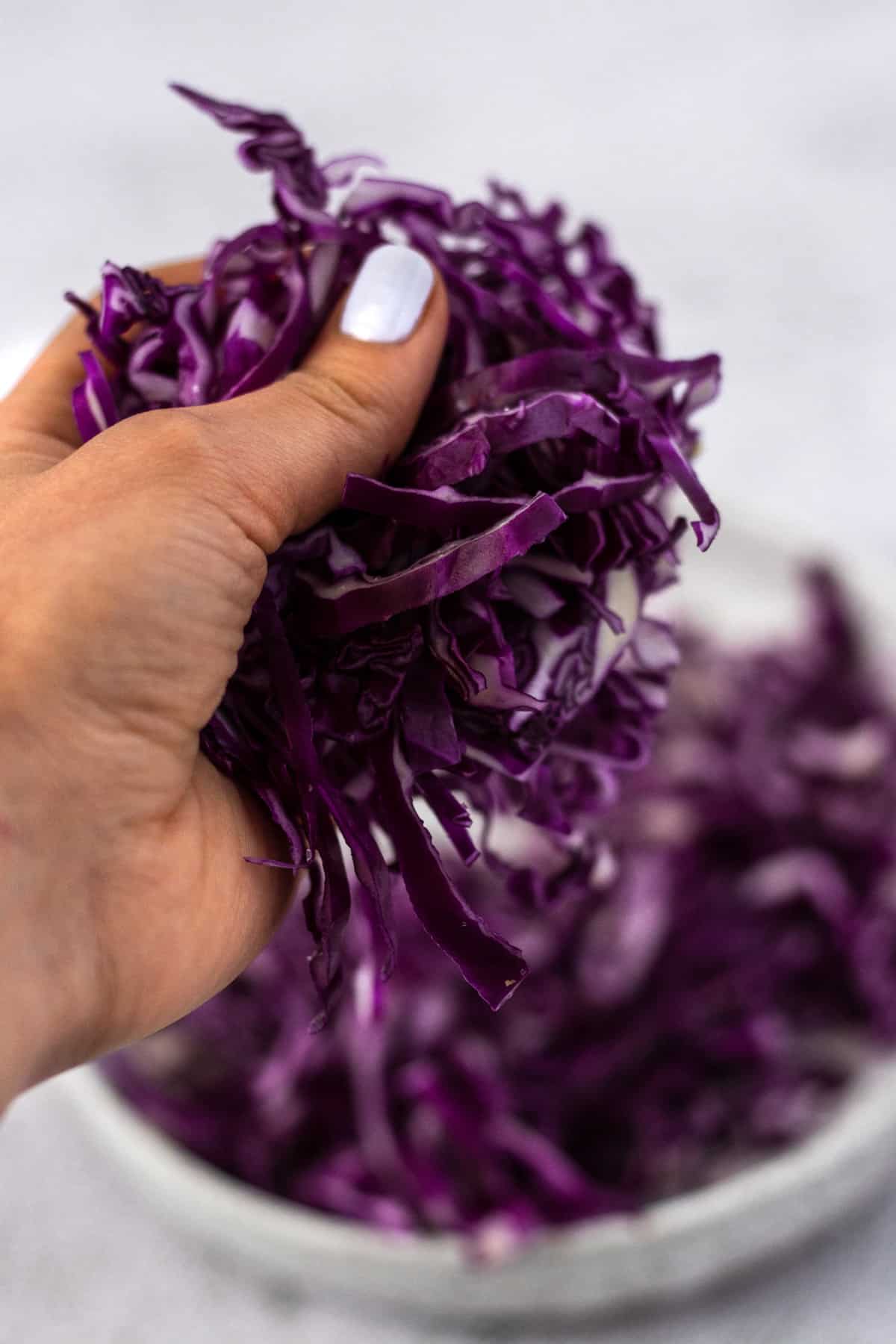 A hand massaging a bunch of shredded red cabbage over a bowl.