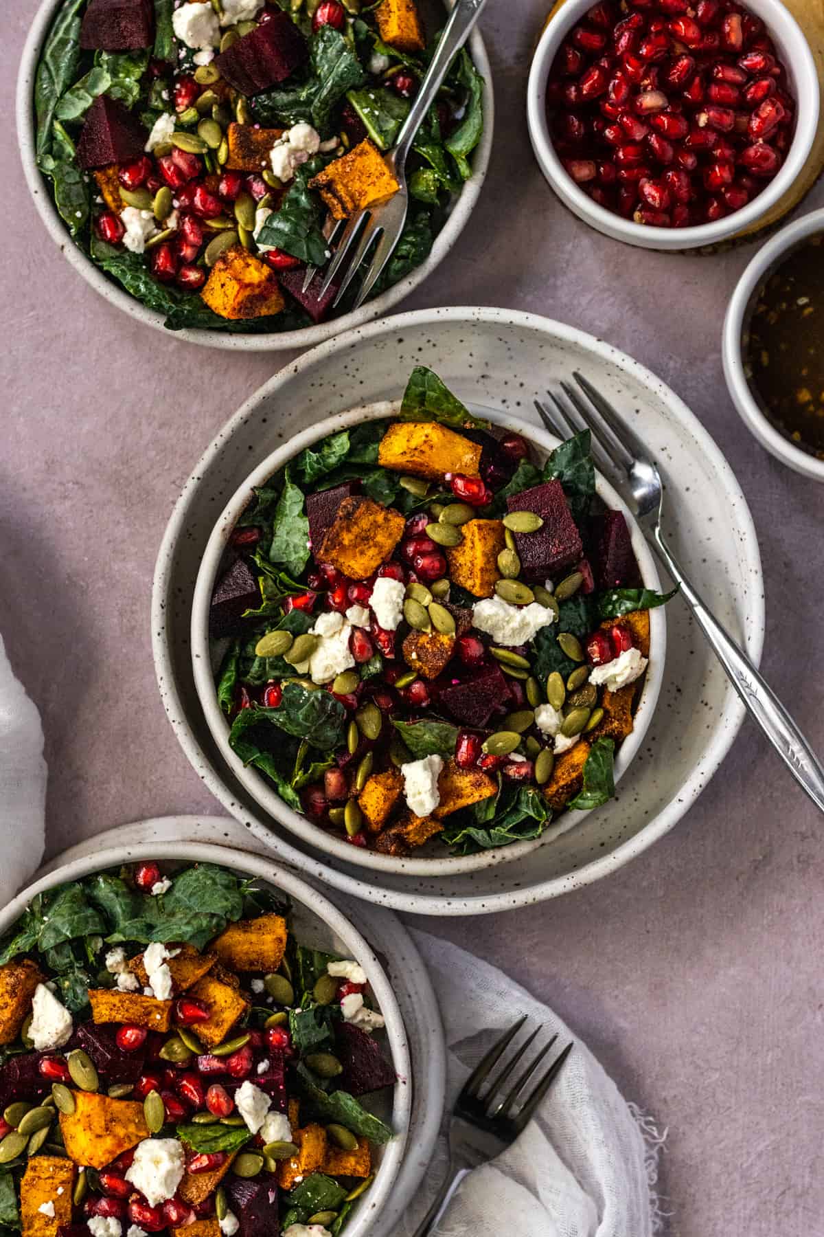 Three bowls of beet and butternut squash salad with forks and pomegranate seeds.