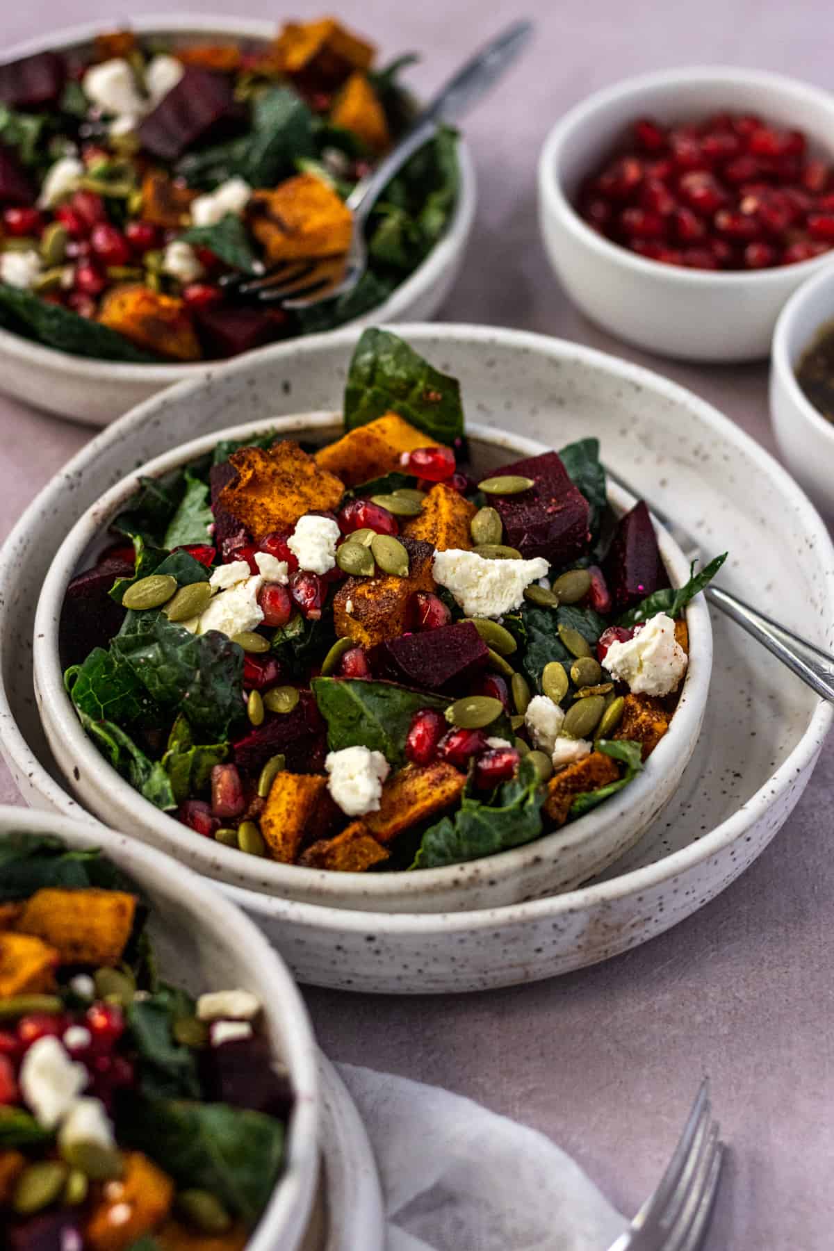 Three bowls of beet and butternut squash salad with forks and pomegranate seeds.
