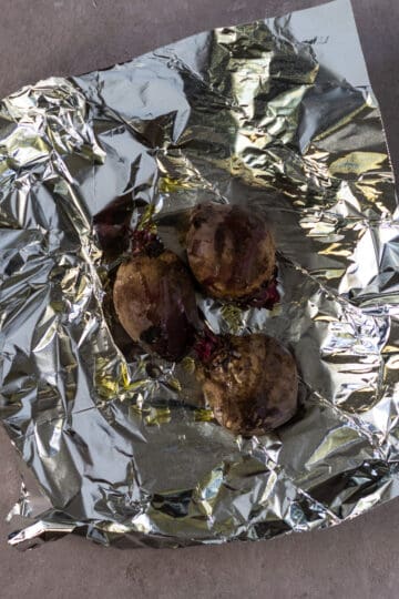 Three purple whole beets on a square of aluminum foil.
