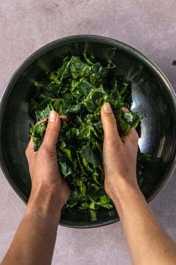 Large mixing bowl of kale being massaged with hands.