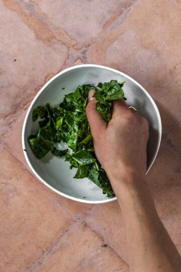 Hand massaging kale in a white bowl.