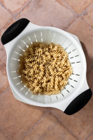 White colander with cooked whole wheat rotini pasta.