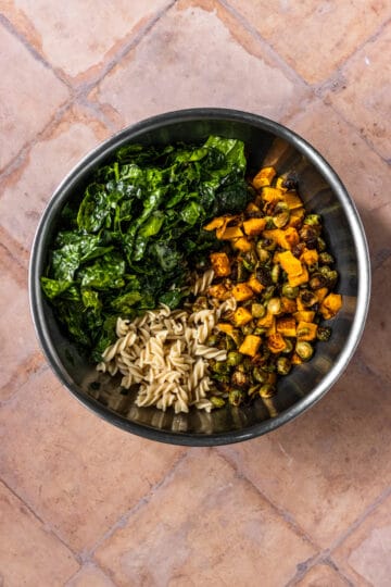 Large bowl with pasta, kale, roasted butternut squash and Brussels sprouts before getting mixed.
