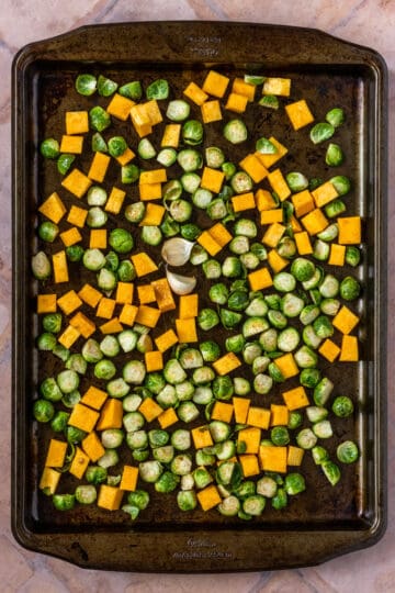 Sheet pan with cubed butternut squash, Brussels sprouts and garlic cloves.
