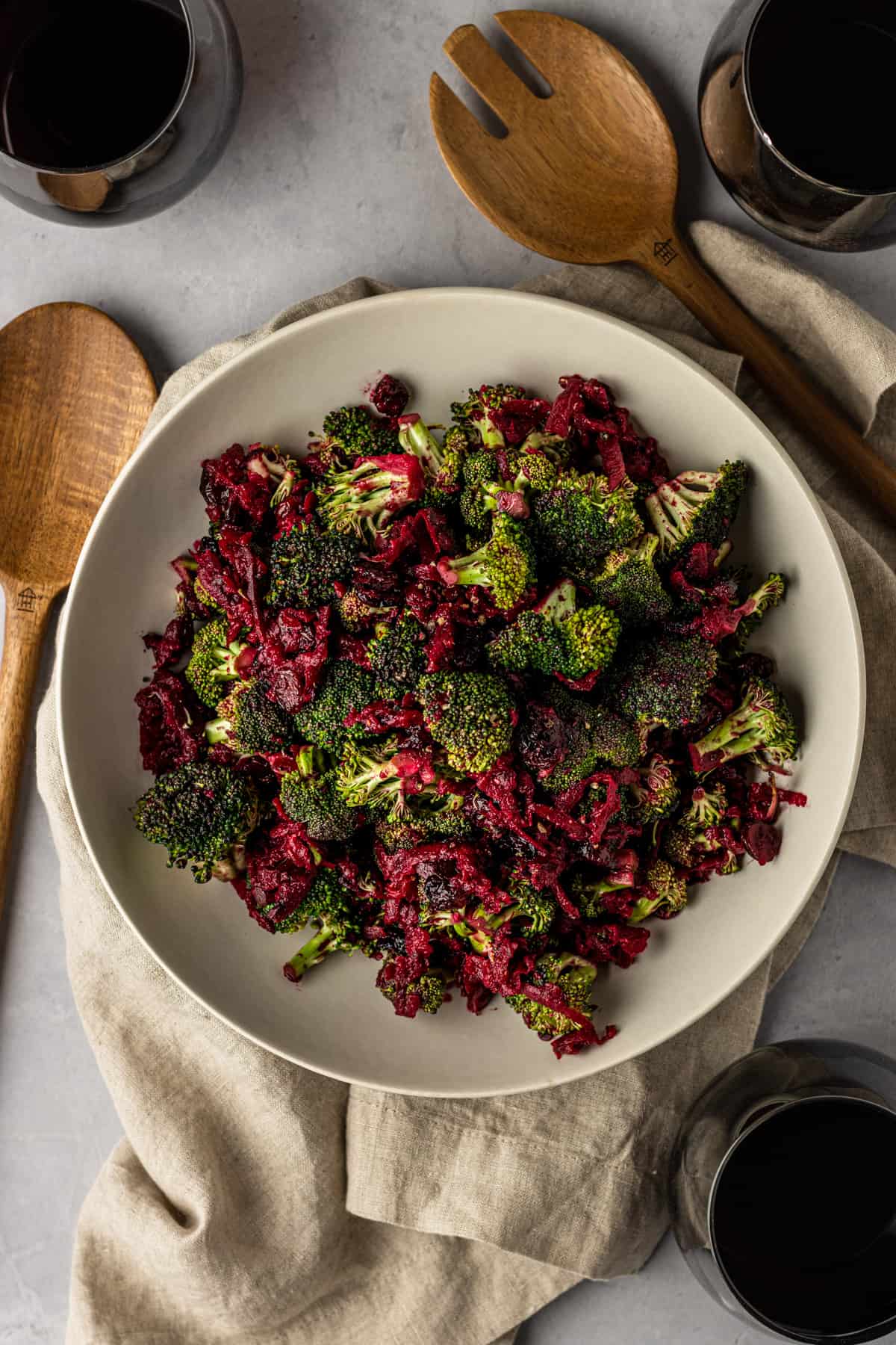 Broccoli beet salad in a large white bowl on a linen cloth with three glasses of wine.