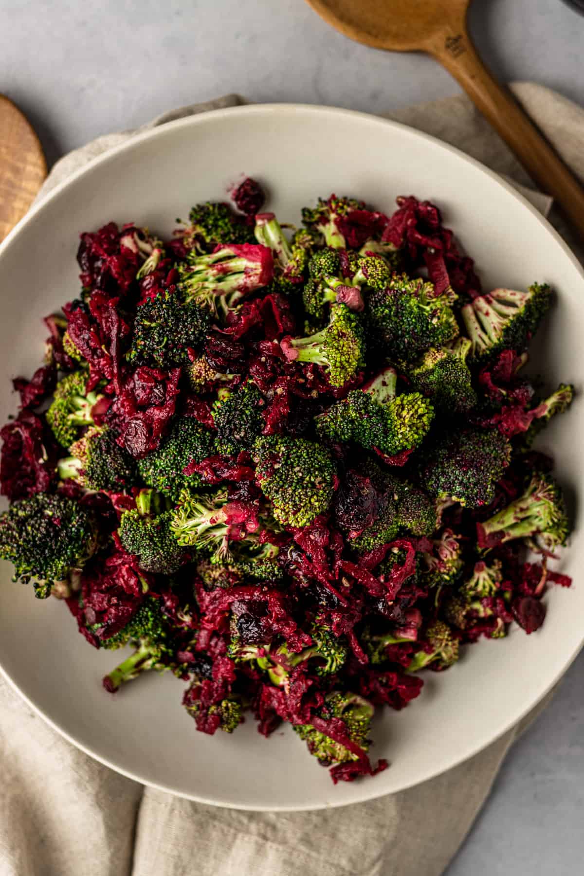 Broccoli beet salad in a large white bowl on a linen cloth and wooden utensils.