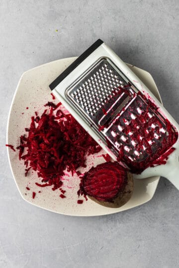 Partially grated beet on a plate with a grater.