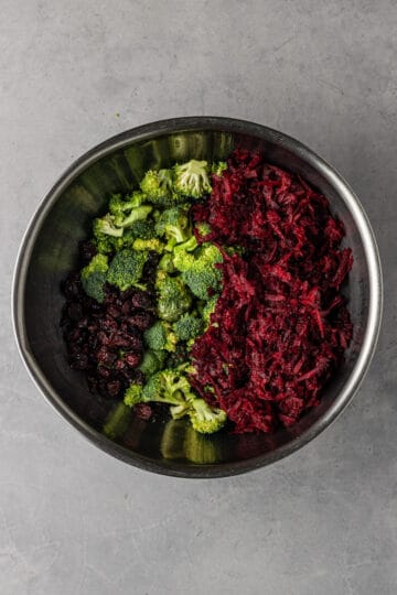 Large metal mixing bowl of broccoli florets, shredded beets and dried cranberries.