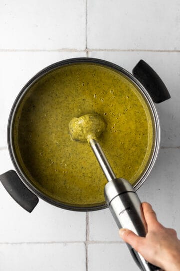 Large pot with broccoli zucchini soup being blended with an immersion blender.
