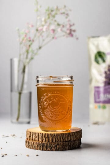 Mason jar filled with honey lavender simple syrup on two wooden coasters with dried lavender and flowers.