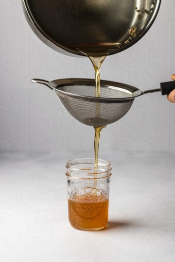 Honey lavender simple syrup being poured from a saucepan and strained into a mason jar.