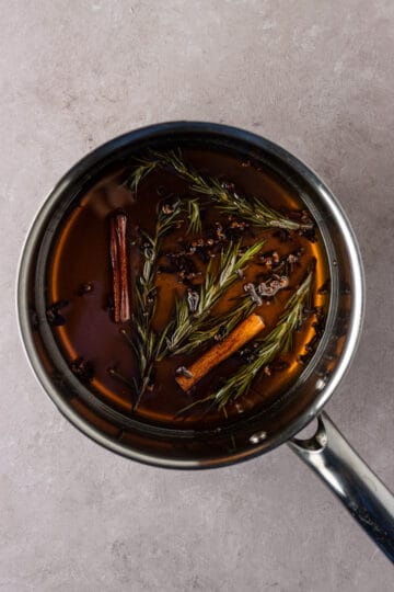 Sauce pan with dissolved light brown sugar, cloves, cinnamon and rosemary.