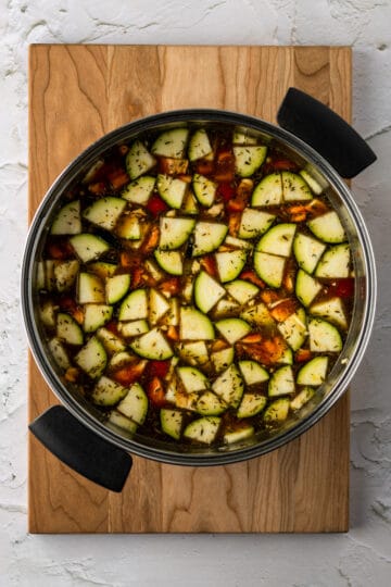 Large pot on a cutting board with sautéed vegetables in vegetable stock broth.