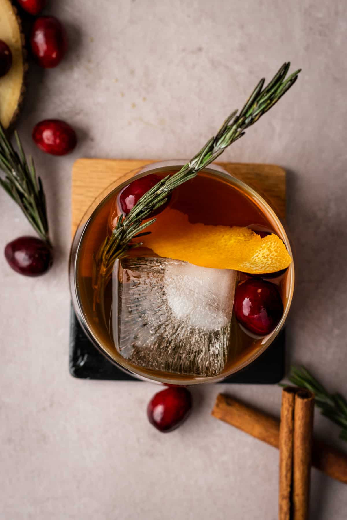 Overhead view of winter old fashioned cocktail on a square coaster garnished with cranberries, rosemary and orange peel.