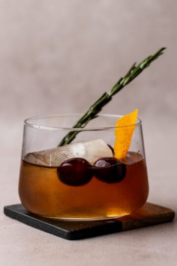 A winter old fashioned in a whiskey glass on a coaster with garnishes.