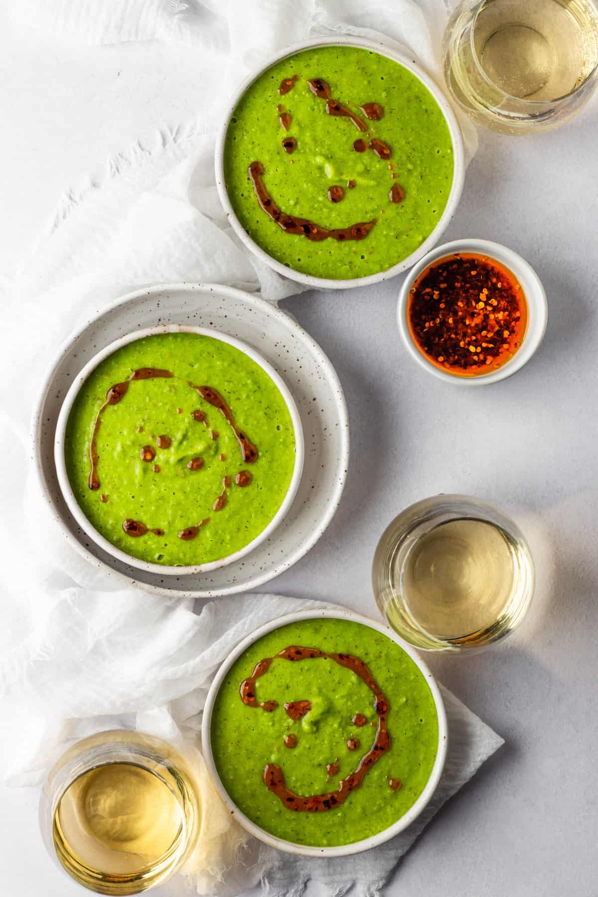 Three bowls of creamy green pea soup with garlic chili oil drizzled on top.