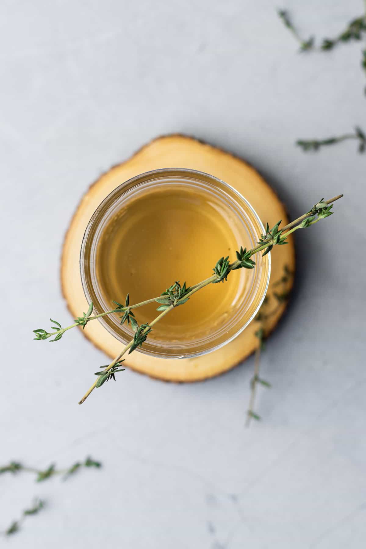 Overhead view of a mason jar on a wooden coaster filled with thyme simple syrup and garnished with thyme leaves.