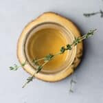 Overhead view of a mason jar on a wooden coaster filled with thyme simple syrup and garnished with thyme leaves.