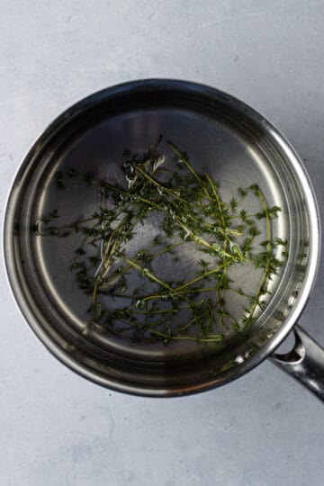 A saucepan with dissolved sugar and water with thyme leaves.