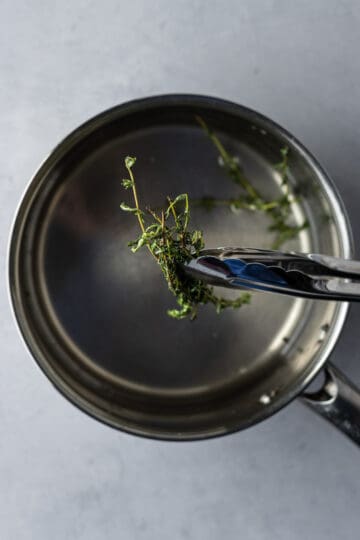 Thyme leaves being removed using tongs from a saucepan.