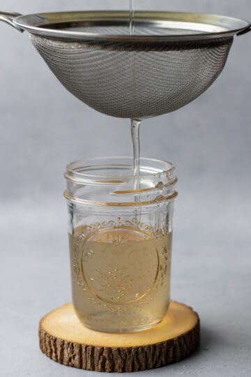 Simple syrup being strained into a mason jar using a fine mesh strainer.