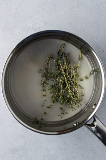 A saucepan with water, sugar and thyme leaves.