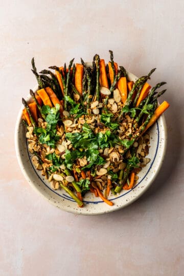 Roasted carrots and asparagus with toasted almonds and parsley on a white plate.