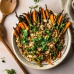Roasted carrots and asparagus with toasted almonds and parsley on a white plate with wooden utensils.