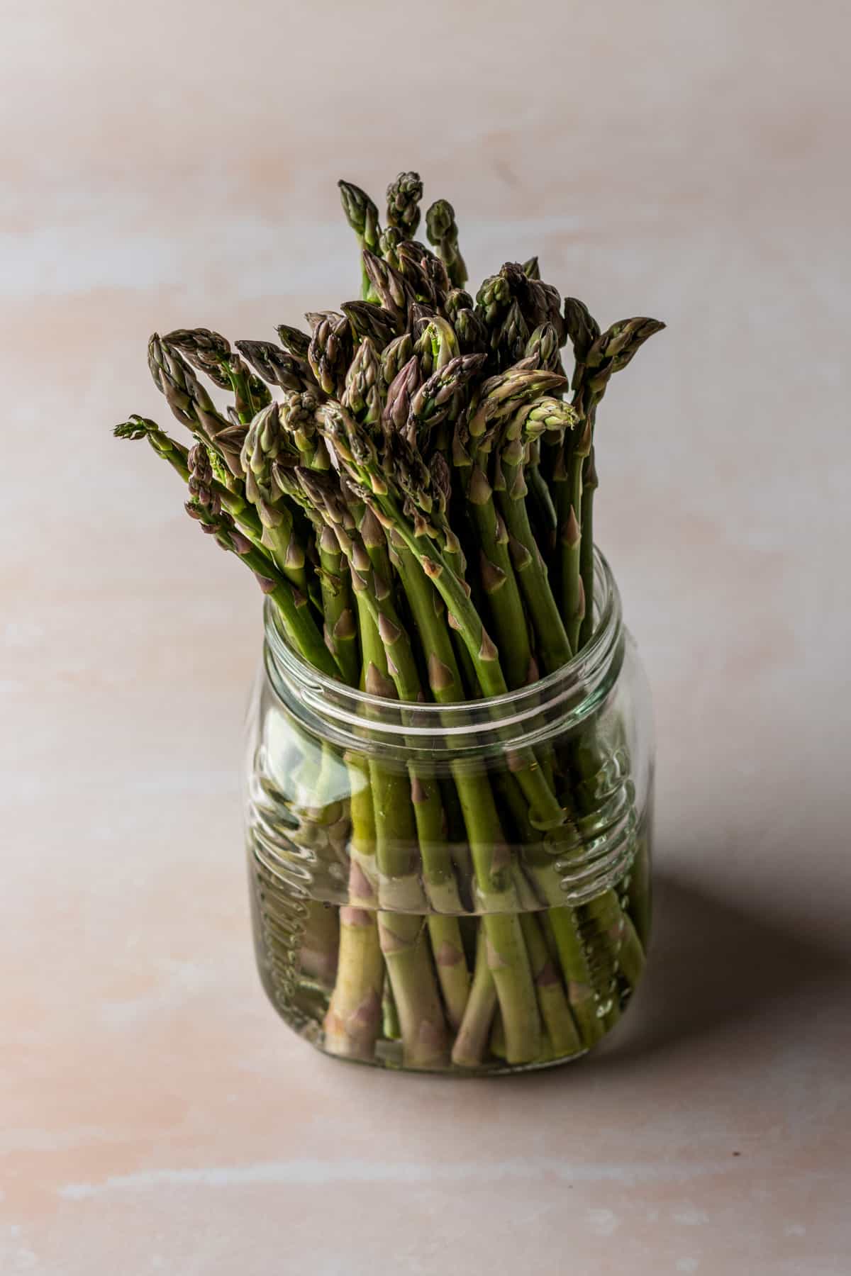 Stalks of asparagus in a large glass jar filled with water.