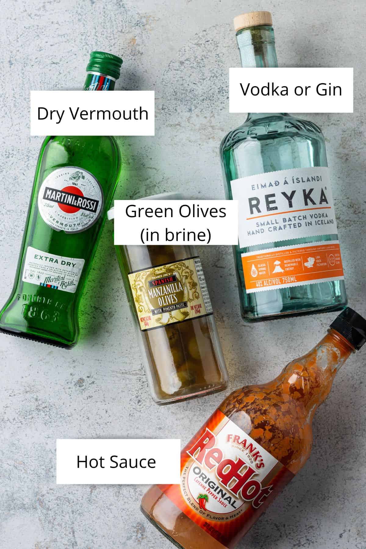 Overhead view of bottles of dry vermouth, vodka, hot sauce and a jar of green olives.