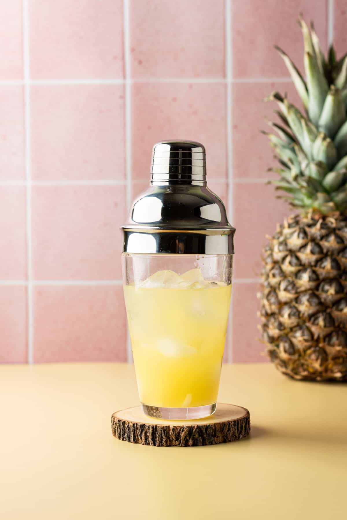 Pineapple juice in a cocktail shaker on a wooden coaster.