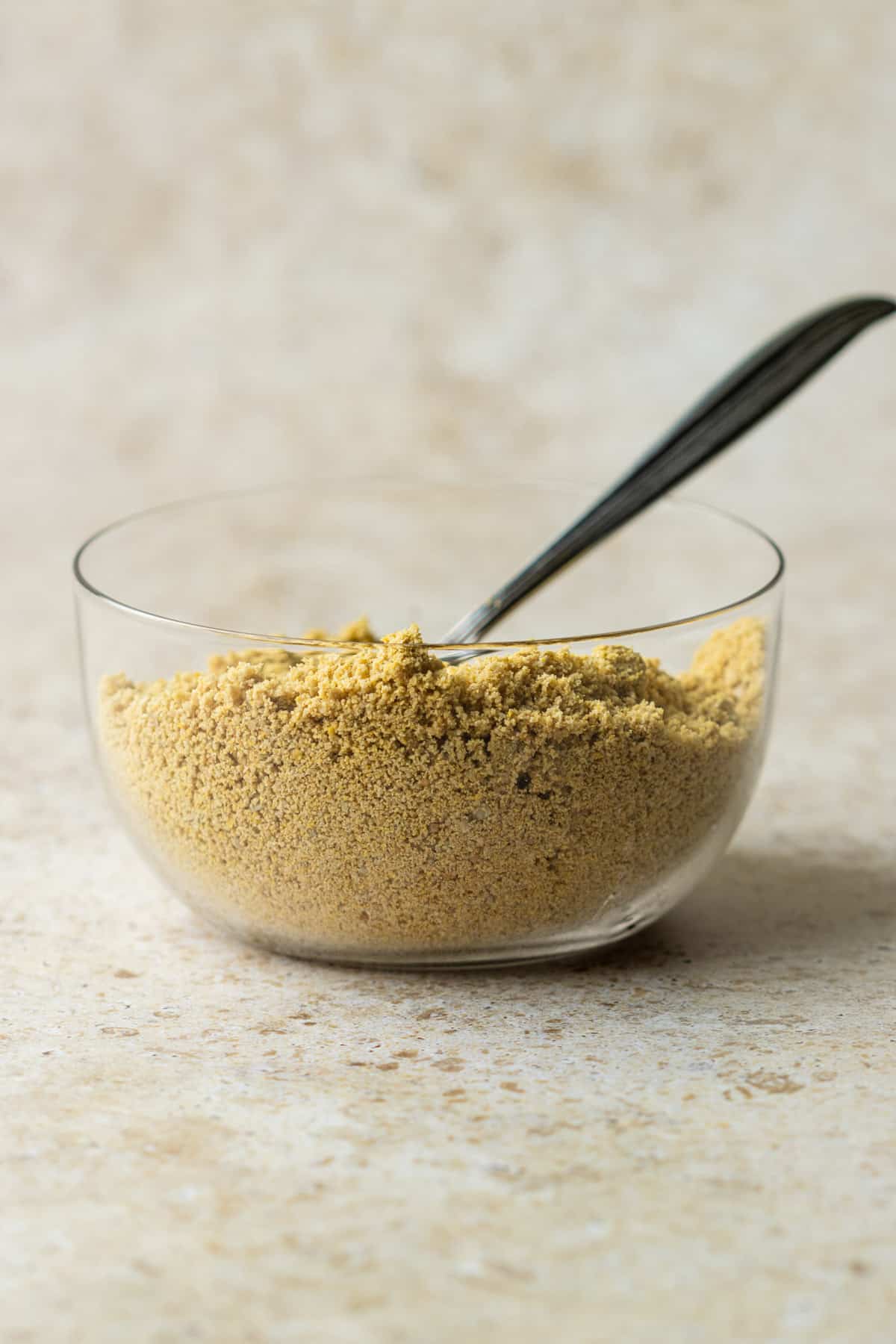 Homemade sunflower seed vegan parmesan cheese in a clear bowl with a spoon.