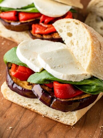 Balsamic grilled eggplant sandwiches with roasted red peppers, basil and mozzarella on a wooden cutting board.