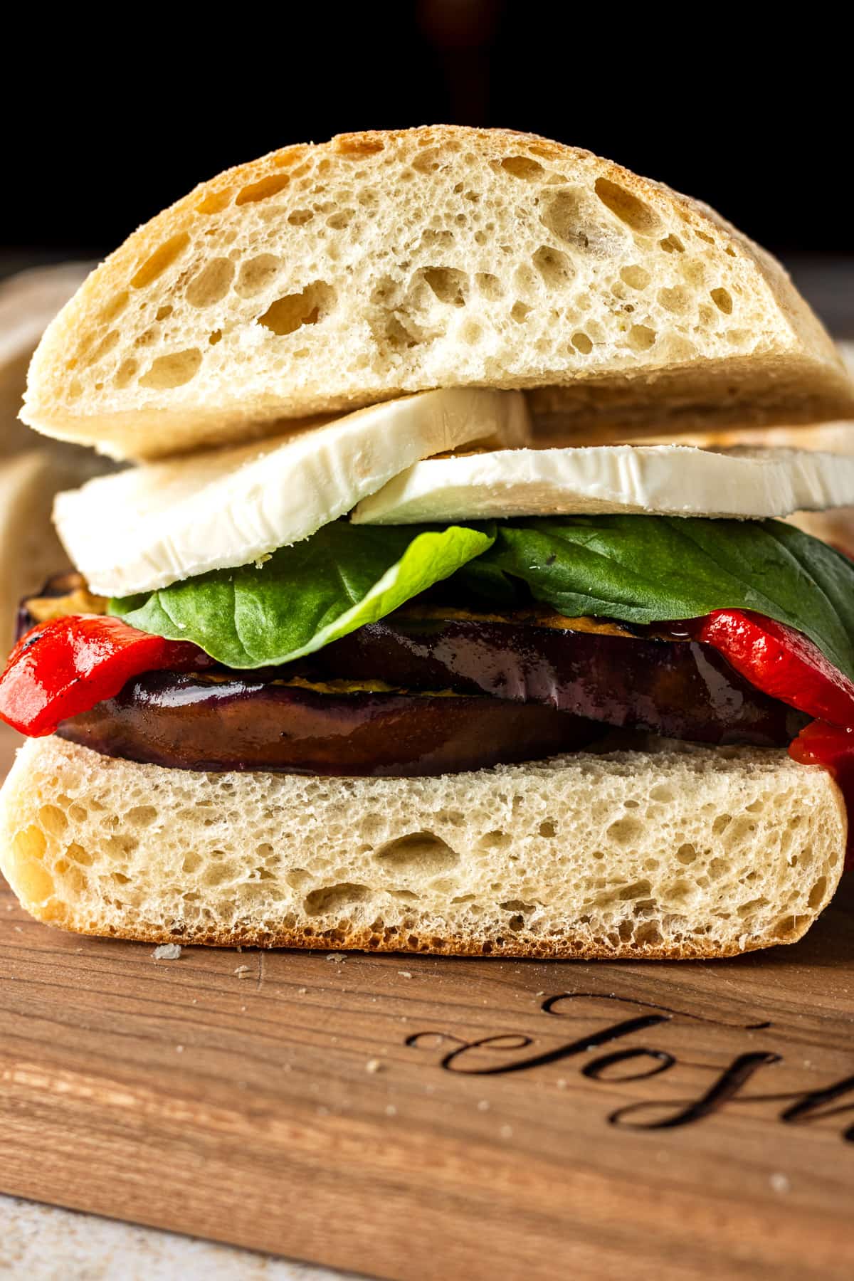 Grilled eggplant sandwich including red pepper, basil and cheese on a wooden cutting board.