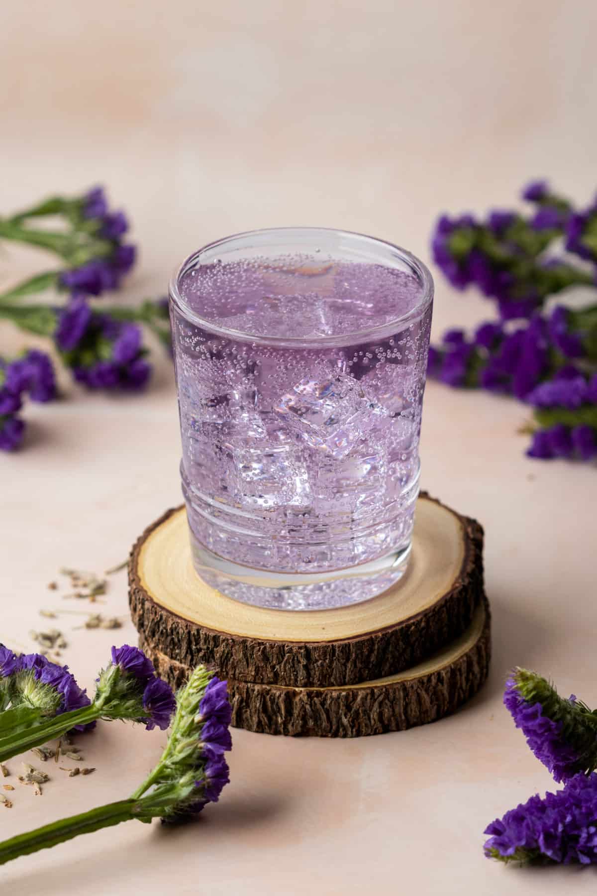 Empress gin and and tonic on two wooden coasters with purple flowers scattered around.
