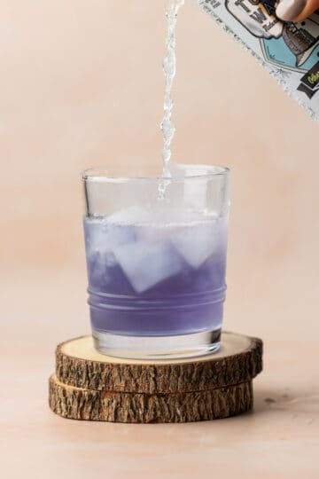 Lavender gin in a glass with ice being topped off with tonic water.