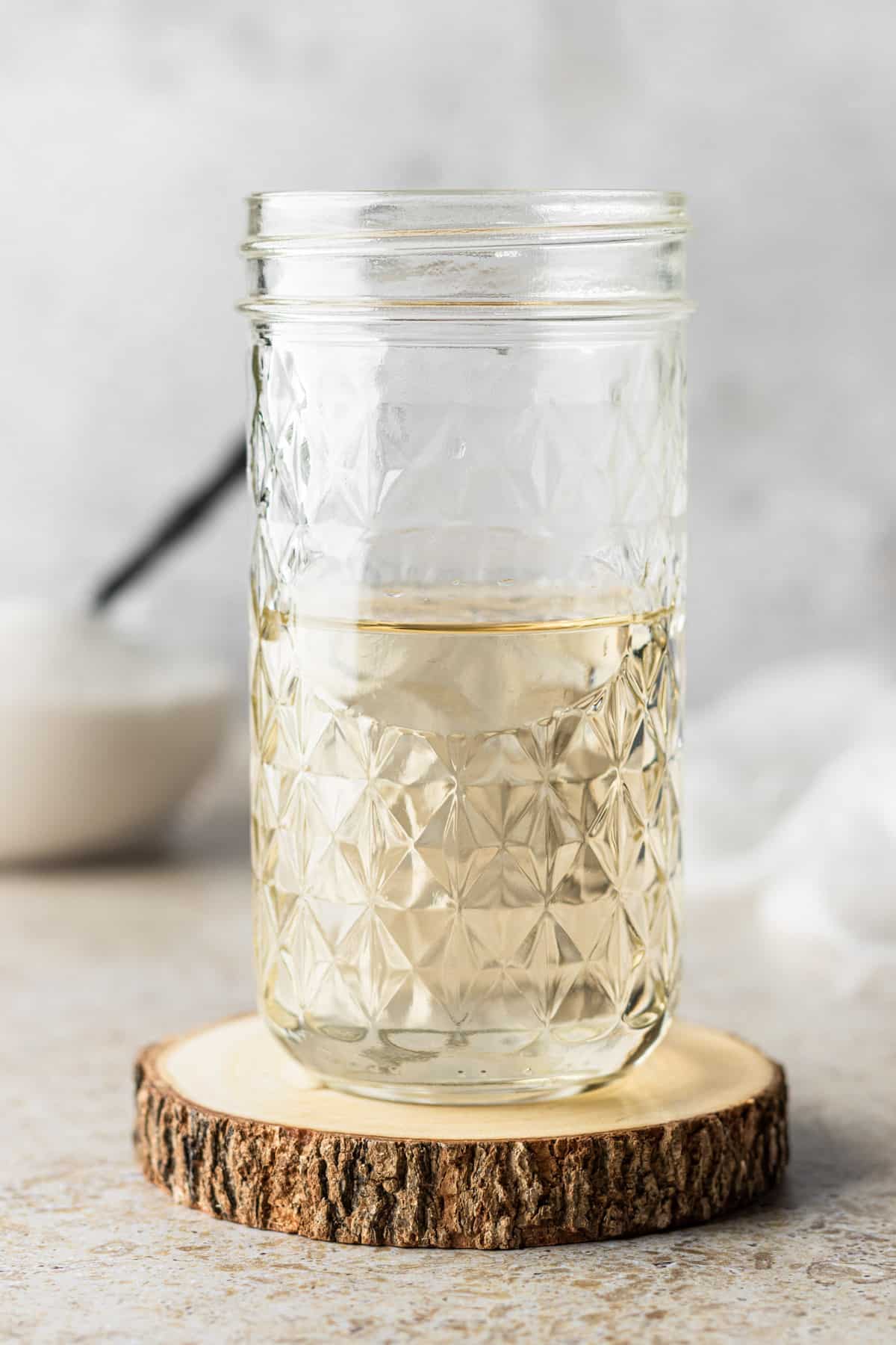 Simple syrup in a tall mason jar on a wooden coaster with a bowl of sugar.