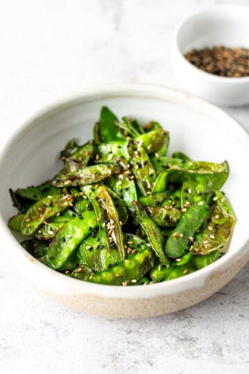 Snow peas in a while bowl garnished with toasted tuxedo sesame seeds.