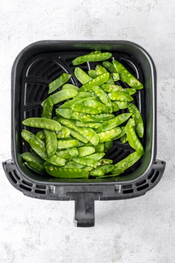 A black air fryer basked with snow peas.